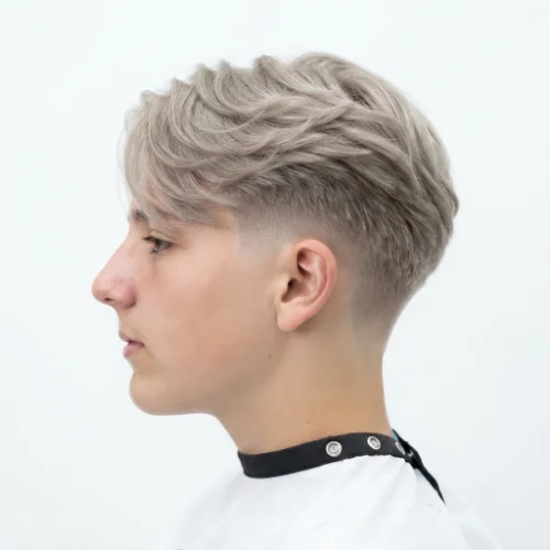 Man with wavy blonde hair and a low taper fade haircut on a white background.